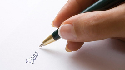 Close up holding a pen, writing dear on the paper