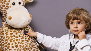 Child dressed up as a doctor examining his stuffed giraffe.
