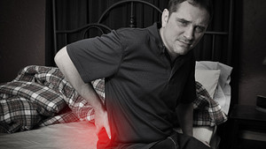 Man sitting on the side of his bed with radiating pain in his lower back